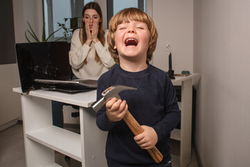 Happy child smashes mom's work laptop to spend more time together. The toddler laughs because he...