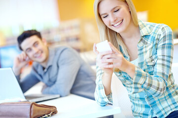 Her mother texted just to see if she was ok. Attractive female student reading a funny text with her study buddy in the background.