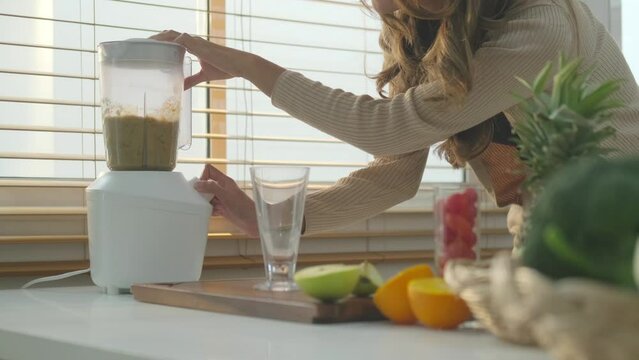Happy young woman making green smoothies with blender in kitchen. Healthy lifestyle and nutrition concept.