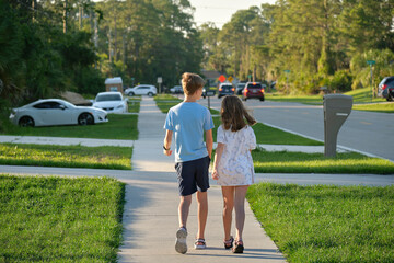 Rear view of two young teenage children, girl and boy, brother and sister walking together on rural street on bright sunny day. Vacation time concept