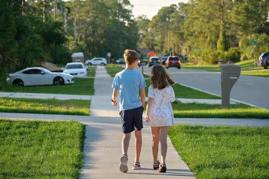 Rear view of two young teenage children, girl and boy, brother and sister walking together on rural street on bright sunny day. Vacation time concept - Powered by Adobe