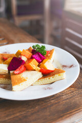Fluffy pancakes with pieces of fruit on a white plate. Delicious breakfast on the wooden table
