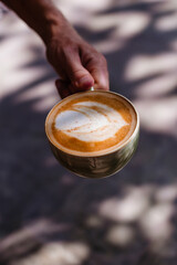 Hand holding coffee with milk in a ceramic cup against the background of the sun's rays. Delicious cappuccino with beautiful foam in the morning