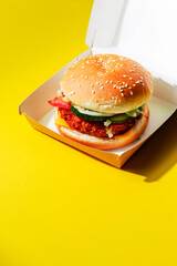 Burger in a paper delivery box on a yellow background with space for text. Stylish burger mockup