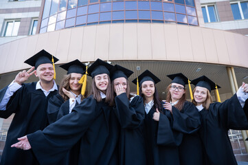 Obraz premium Happy students in graduate gown stand in a row against the backdrop of the university. 