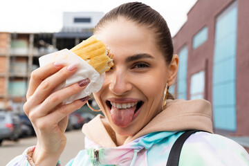 Young Slim brunette girl eating fast food hotdog or burger outdoor on the street.