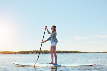 It makes her feel calm. an attractive young woman paddle boarding on a lake.