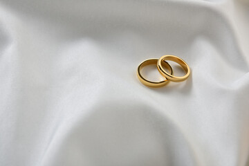 Gold rings on white shiny fabric top view