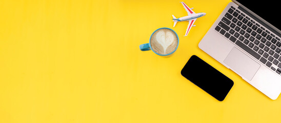 Travel flatlay. Laptop, coffee, phone and plane on yellow background with copy space. Planning summer vacation concept. Summer workspace.