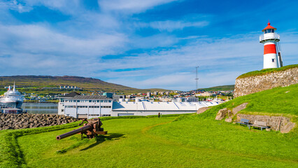 Fototapeta na wymiar Torshavn, Faroe Islands - Lighthouse, old military fortress Skansin with cannons, WWII guns and tourists in the modern capital Torshavn of Faroe islands