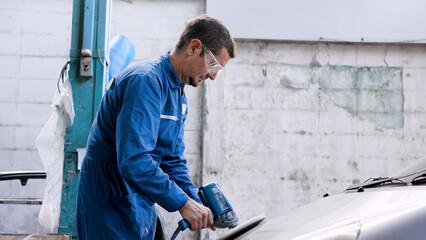 Hand male mechanic wearing suit for working in garage for safety in risky work, wear dustproof goggles, mechanic standing using polishing machine scrub surface car that comes garage make new color.