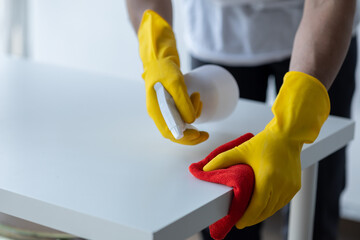 Person cleaning the room, cleaning staff is using cloth and spraying disinfectant to wipe the table in the company office room. Cleaning staff. Maintaining cleanliness in the organization.