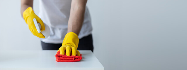 Person cleaning the room, cleaning staff is using cloth and spraying disinfectant to wipe the table in the company office room. Cleaning staff. Maintaining cleanliness in the organization.