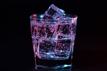 Glass of cold water with ice with colored lighting on a black background. refreshing drink