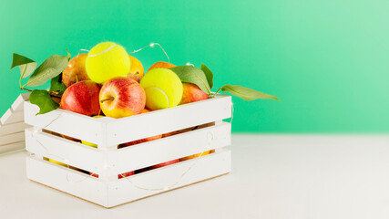 Tennis composition with yellow tennis balls, apples in a white wooden box with lightening on white...