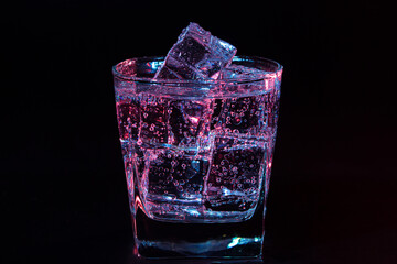 Glass of cold water with ice with colored lighting on a black background. refreshing drink