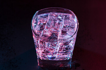 Glass of cold water with ice with colored lighting on a black background. refreshing drink