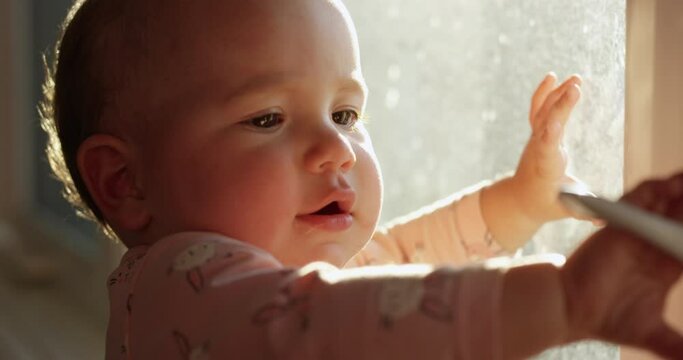 Toddler girl trying to open window on sunny morning - close up on face