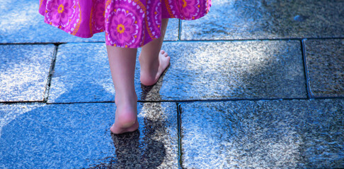 Little adorable child girl walking barefoot along a wet street and have fun in outdoor water...