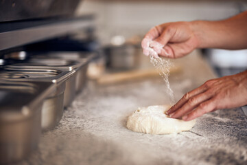 A male pizza master sprinkles flour over the pizza dough in the kitchen.