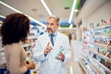 Obraz premium A senior male pharmacist is talking with a female customer about some product in the apothecary.
