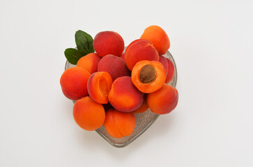ripe apricots in a heart-shaped bowl on a white background flat lay