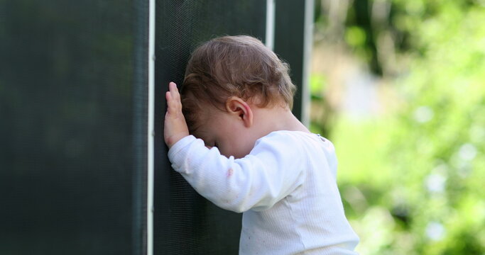 Baby toddler standing next to pool fence outside. Pool barrier prevention