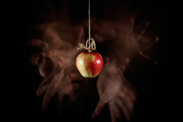 Wiszące na sznurku czerwone jabłko z chciwymi dłońmi wokół - obrazy, fototapety, plakaty