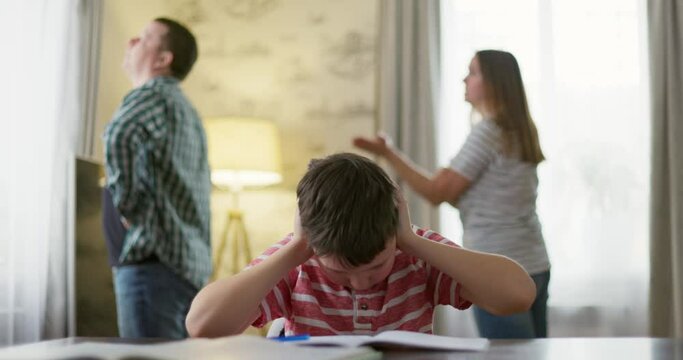 Sad child covers his ears with his hands during an argument between his parents