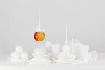 Wiszące na sznurku czerwone jabłko nad plastikowymi jednorazowymi naczyniami  - obrazy, fototapety, plakaty