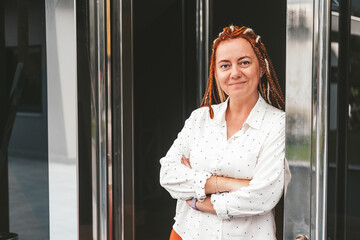 A modern middle-aged woman with a bright hairstyle stands in the doorway of a business center and smiles. 