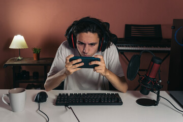 teenage gamer or streamer very concentrated playing mobile games on his smartphone very close to his face and with a facial expression of concentration.	
