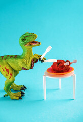 A cute little green dinosaur holds a fork and knife near a table with a roast turkey.