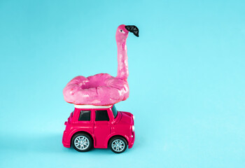 Vintage pink car with inflatable flamingo on a roof on a blue background. Miniature toys. Creative summer advertisment poster.