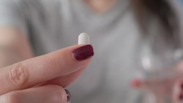 Woman taking white pill of statin medicine to treat high cholesterol or painkiller with glass of water. Taking medicine