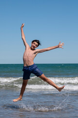 Fototapeta na wymiar Happy boy performs pirouettes and big jumps on the seashore during his summer vacation on the Atlantic Coast, Las Grutas, Rio Negro, Argentina.