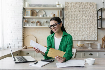 Smiling young woman working at home with laptop and documents. He opens the letter from the...