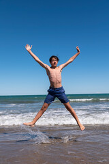 Young man jumping on the sea shore happy in his summer vacation.