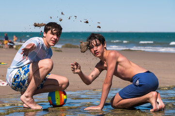 Amigos jugando a realizar pozos en la playa, tirando la arena al aire libre, totalmente relajados...