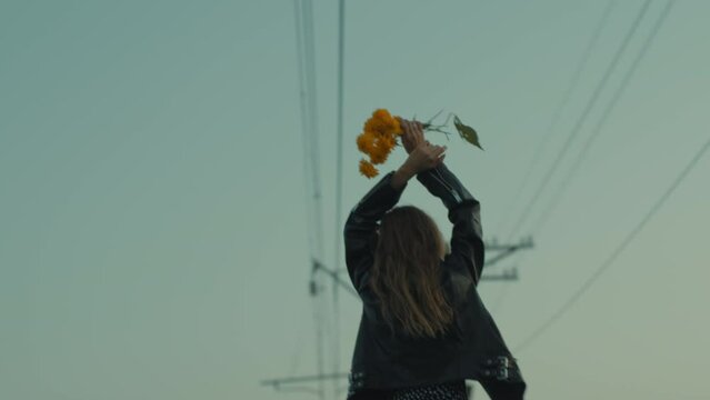 A young woman with yellow flowers dances at the evening sky.
