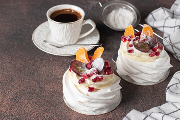 Mini Pavlova cake with pomegranate, tangerines and grapes on brown background