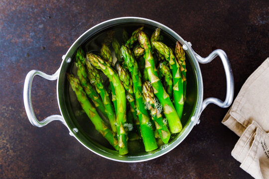 Boiled asparagus with water in a pot on a table. Preparing healthy food concept.