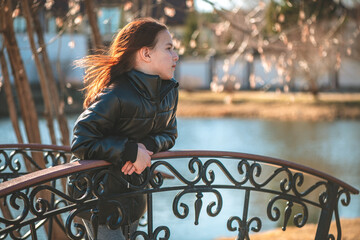 pensive girl of school age stands on the bridge and looks into the distance
