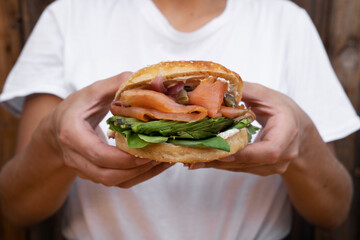 Eating. Closeup view of a woman holding a smoked salmon sandwich with her hands. Delicious layers...