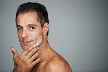 Fototapeta premium Its a face-off with age. Studio portrait of a handsome mature man applying moisturizer to his skin.