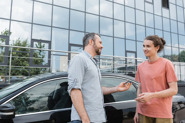 happy bearded man giving car key to teenage son near automobile.