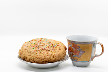 Cookie with colored sprinkles on a plate next to a cup of milk, selective focus