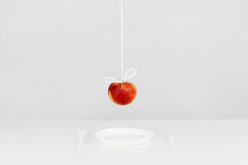 Wiszące na sznurku czerwone jabłko nad plastikowym jednorazowym talerzy ze sztućcami - obrazy, fototapety, plakaty