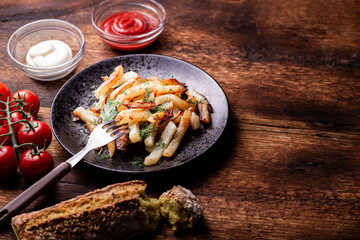 Delicious fried chopped potatoes with ketchup, mayonnaise and herbs on a wooden background.