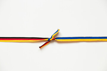 Two ribbons of the flags of Ukraine and Germany are tied in a knot on a white background, friendship and union